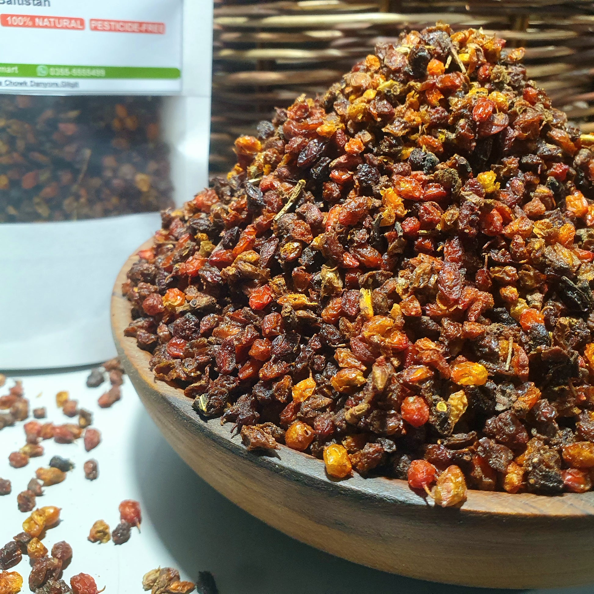 A close-up of dried Sea Buckthorn berries piled in a wooden bowl, with a partially visible branded packet in the background and a woven surface underneath.